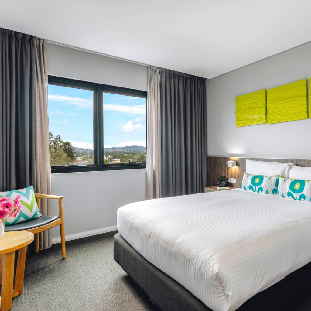 Light-filled hotel room with comfortable queen bed and scenic window views, designed for a relaxing stay
