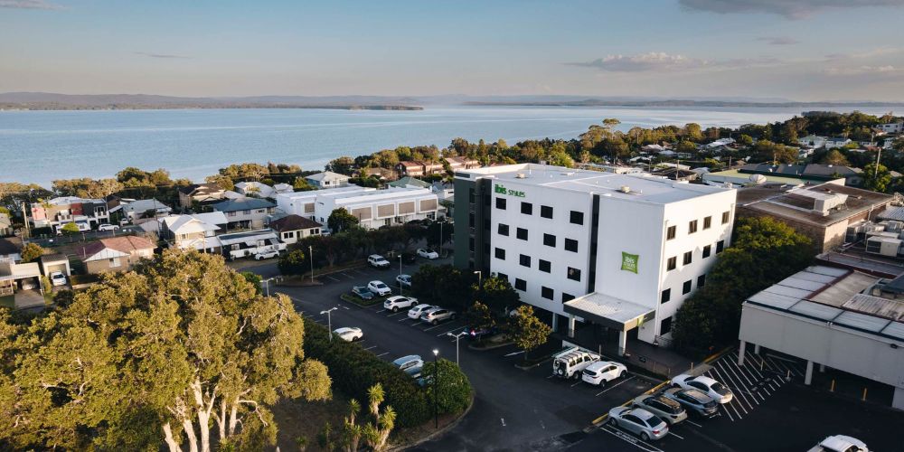 Aerial view of ibis Styles The Entrance showcasing the hotel, on-site parking and prime waterfront location near Tuggerah Lake on the Central Coast of NSW.