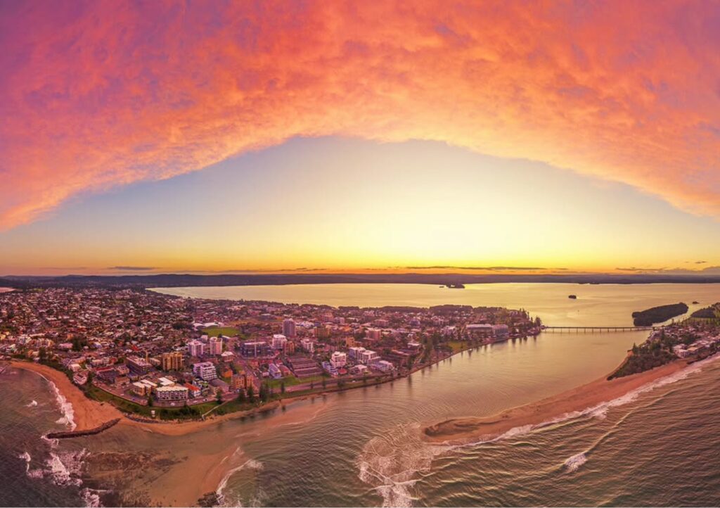 Aerial view of The Entrance at sunset, with vibrant orange and pink skies above the coastline, channel, beaches and waterfront foreshore on the NSW Central Coast.