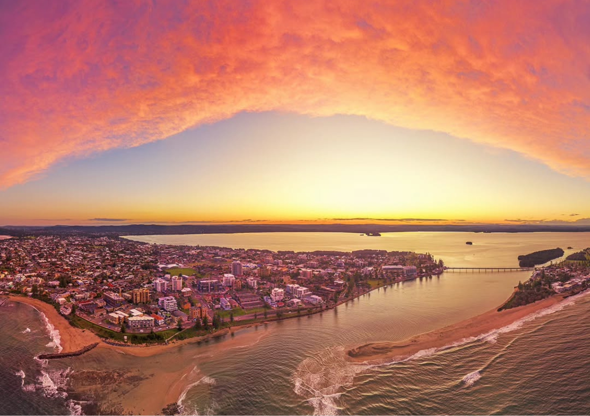 Aerial view of The Entrance at sunset, with vibrant orange and pink skies above the coastline, channel, beaches and waterfront foreshore on the NSW Central Coast.
