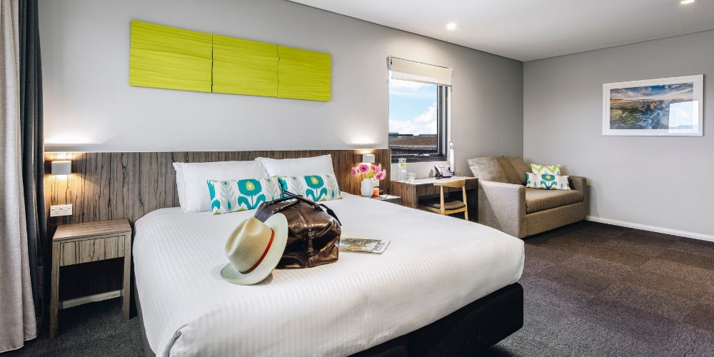 Modern guest room at ibis Styles The Entrance featuring a king bed, comfortable lounge, work desk and contemporary furnishings.