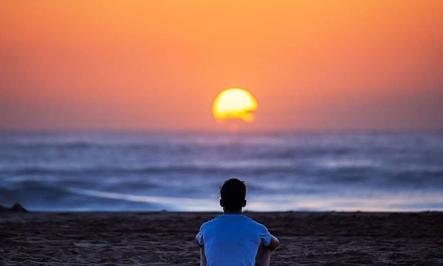 Person sitting on a beach watching the sun rise over the ocean on the NSW Central Coast, Australia.