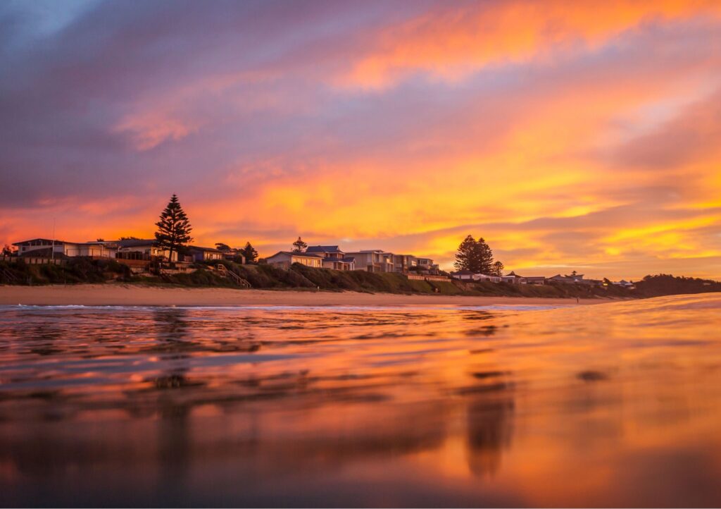 Vibrant orange sunset over Terrigal Beach on the NSW Central Coast, with beachfront homes and reflections across the water.