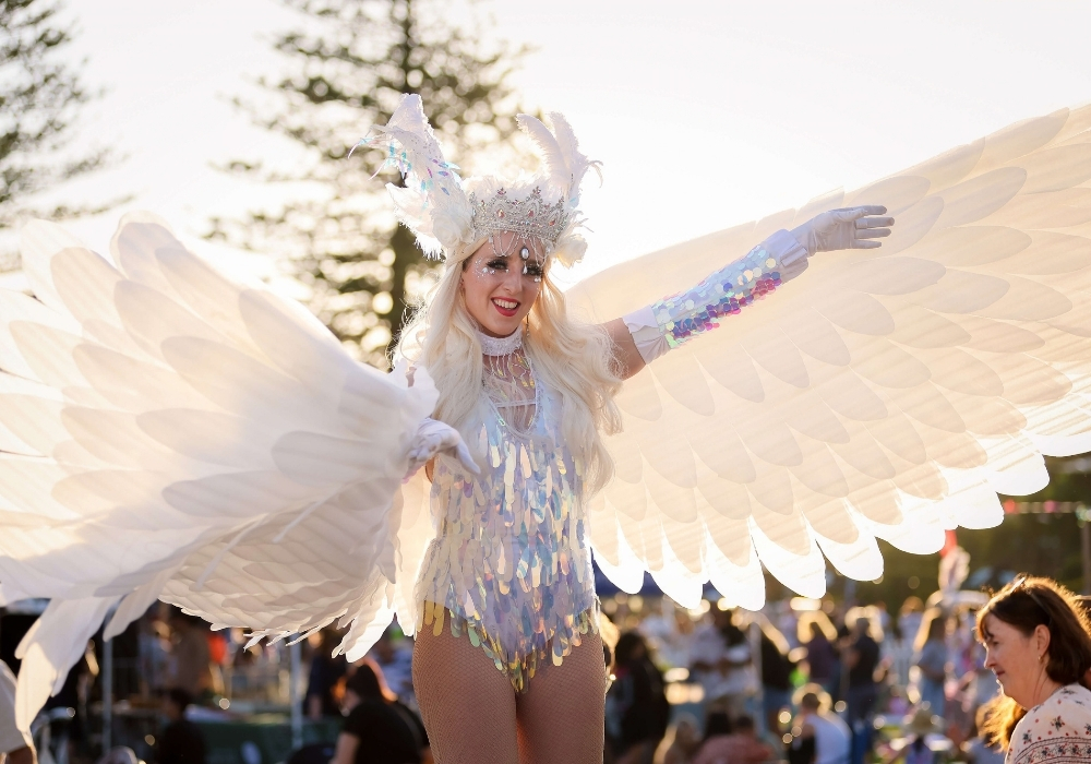 Costumed performer with large white wings entertaining crowds at The Lakes Festival on the Central Coast.